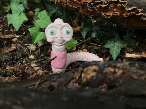 Pink worm-like plasticine character among plants
